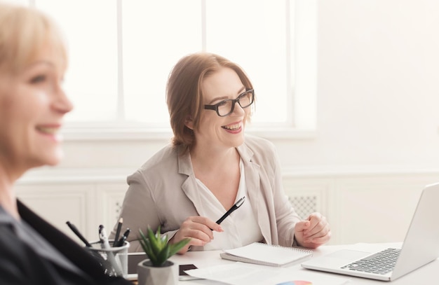 Two happy women working on laptop together in modern office