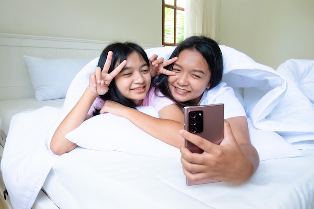 Two happy young girl playing mobile phone on bed in bedroom