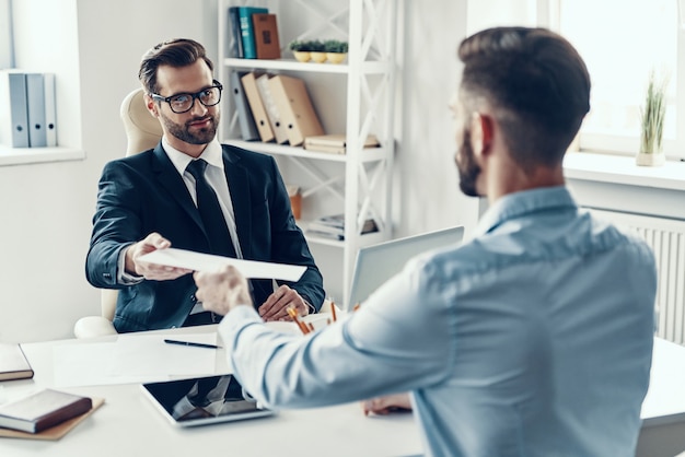 Two happy young men in formalwear communicating together while sitting in the office