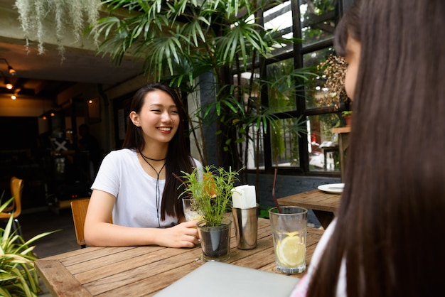 Two happy young teenage Asian women relaxing together at the coffee shop