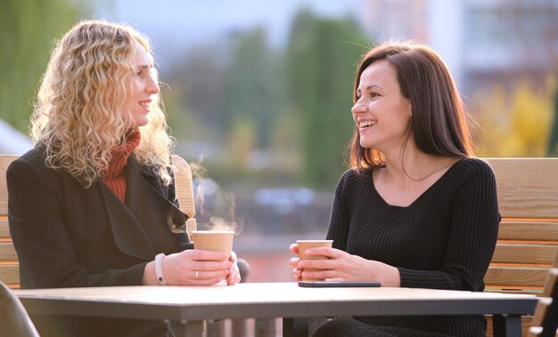 Two happy young women sitting at city street cafe havinh fun\
time together during coffee break.