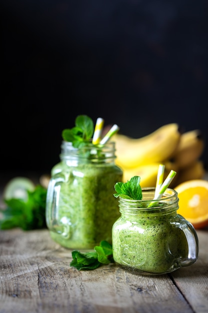 Photo two healthy green smoothies with spinach, banana, orange and mint in glass jar and ingredients. detox, diet, healthy, vegetarian food concept. copy space