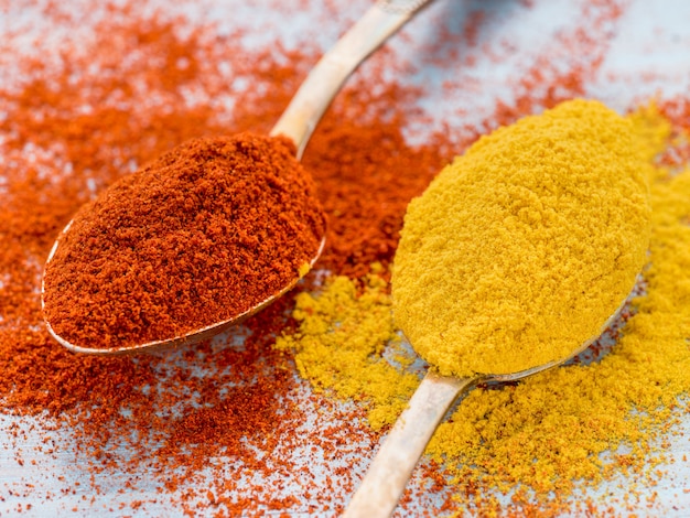 Two heaping scoops of spices of paprika powder and turmeric, curry, powder scattered on th