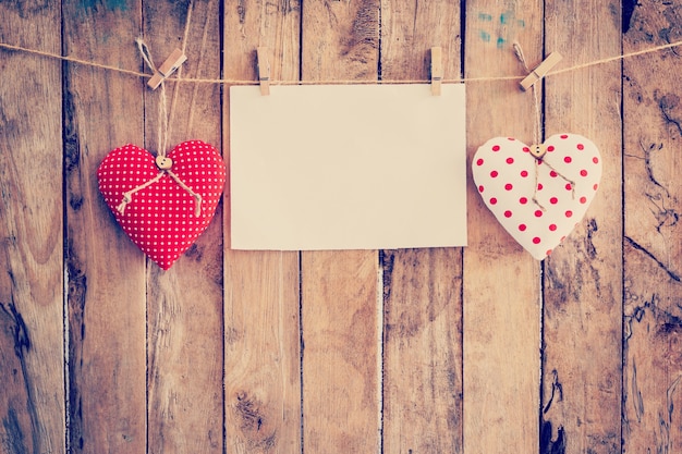 Two heart fabric and paper hanging on clothesline at wood background with space.