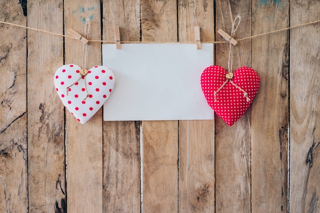 Two heart fabric and paper hanging on clothesline at wood background with space.