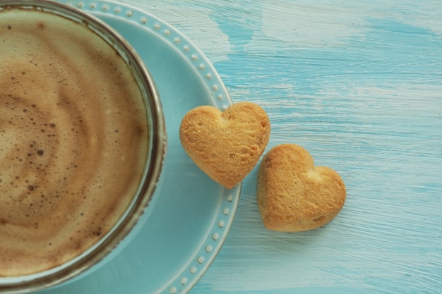Due biscotti a forma di cuore su un piattino vicino a una tazza di caffè.