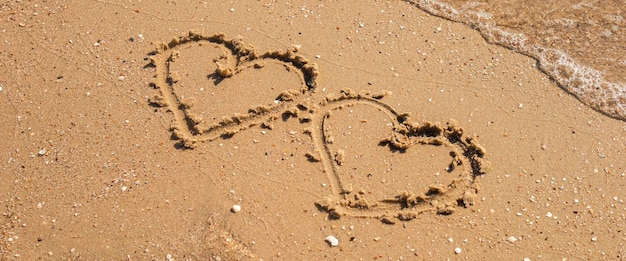 Two hearts drawn on a sandy beach Top view flat lay Banner