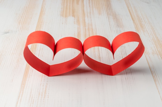 Two hearts made of ribbon on wooden background.