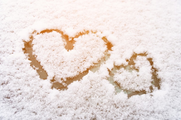 Два символа сердца, нарисованные в белом снегу на лобовом стекле автомобиля зимой