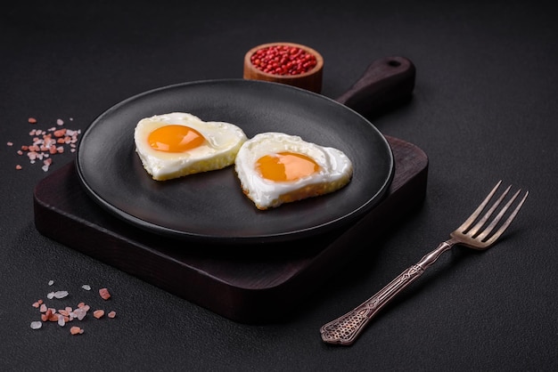 Two heartshaped fried eggs on a black ceramic plate on a dark concrete background