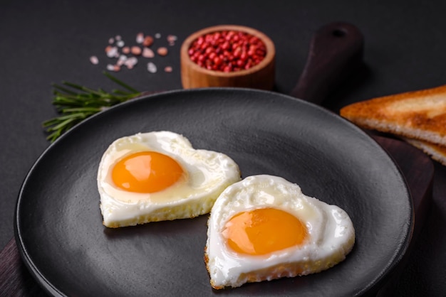 Two heartshaped fried eggs on a black ceramic plate on a dark concrete background