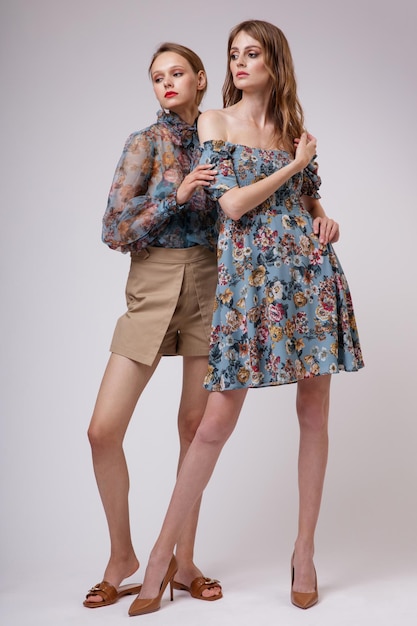 Two high fashion models in blue transparent blouse with floral pattern dress beige shorts