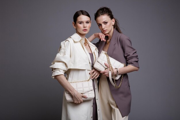 Two high fashion models in white coat  purple jacket top pants accessories handbags