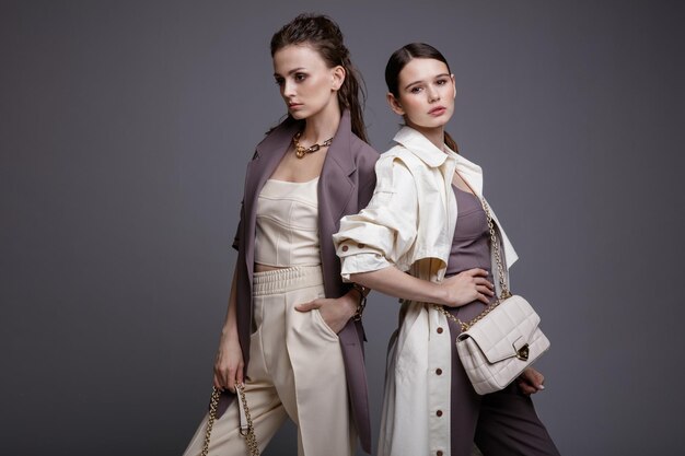 Two high fashion models in white coat  purple jacket top pants accessories handbags