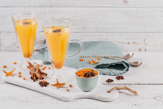 Two high glasses with colorful hot sea buckthorn tea with cinnamon sticks anise stars and fresh sea buckthorn berries