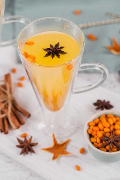 Two high glasses with colorful hot sea buckthorn tea with cinnamon sticks anise stars and fresh sea buckthorn berries