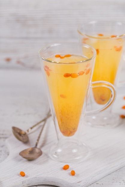 Two high glasses with colorful hot sea buckthorn tea with fresh sea buckthorn berries