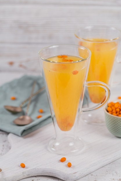 Two high glasses with colorful hot sea buckthorn tea with fresh sea buckthorn berries