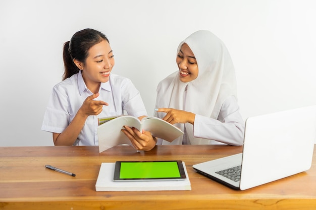 本を見て机に座っている 2 人の女子高生