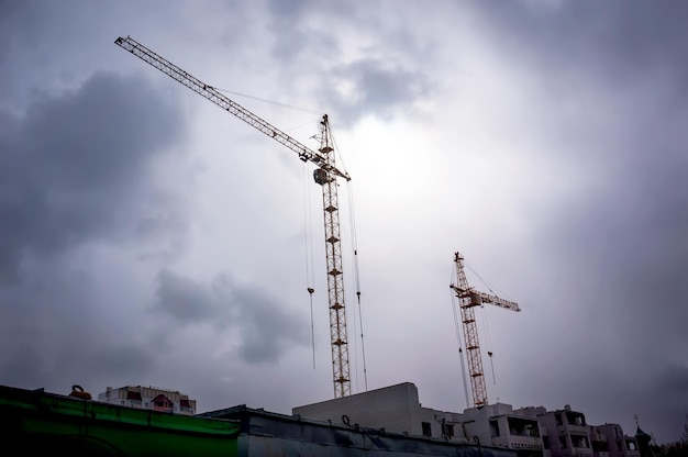 Due alte gru a torre e costruzione in costruzione contro il cielo scuro