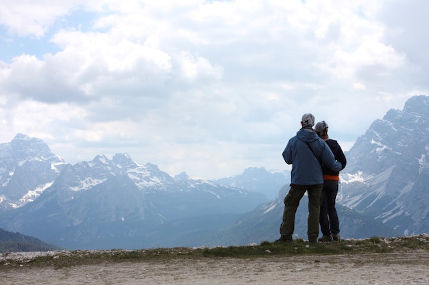 Two hikers are standing on a rock and looking at the  mountains