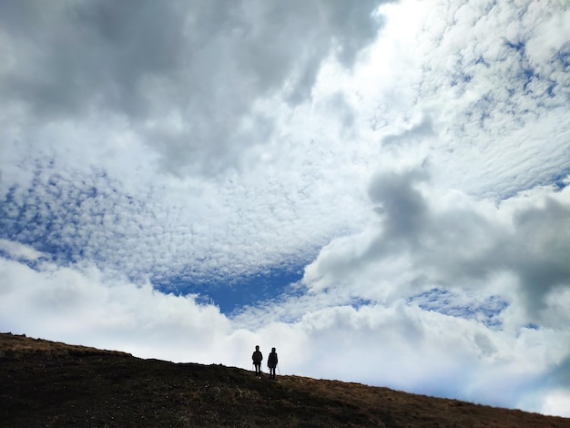 Photo two hikers silhouette in mountains on cloudy sky background