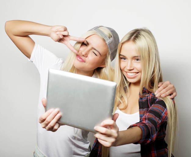 two hipster girls friends taking selfie with digital tablet studio shot over gray vackground