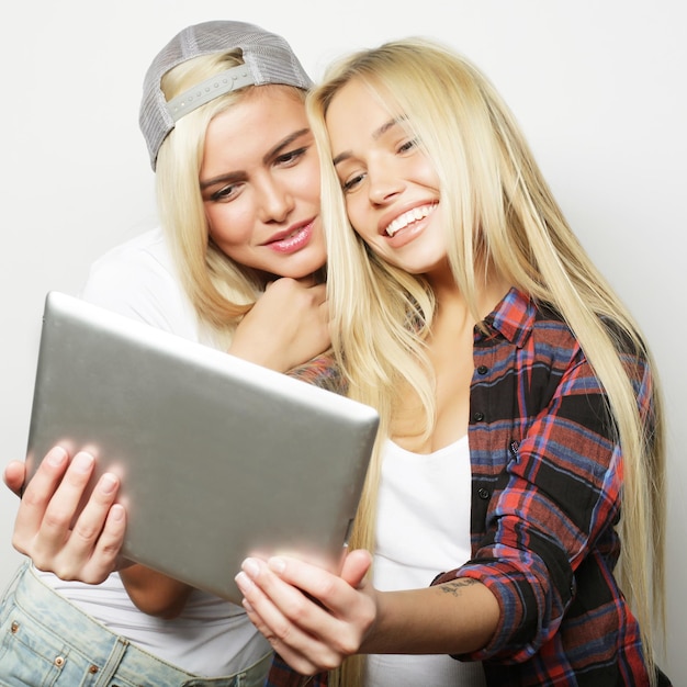 two hipster girls friends taking selfie with digital tablet studio shot over gray vackground