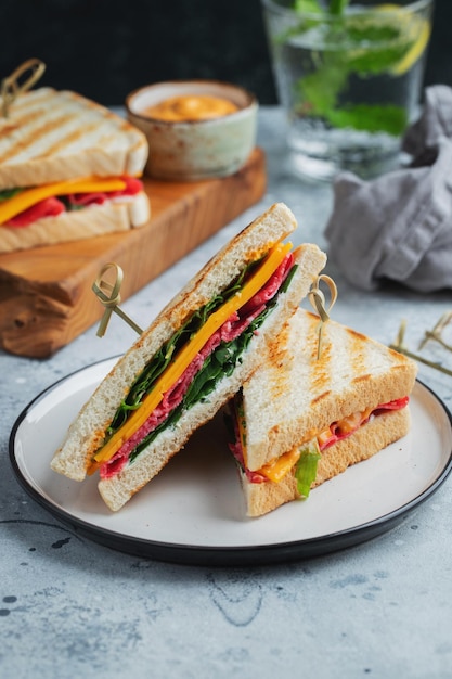 Two homemade sandwiches with sausage cheese and arugula on a light concrete background