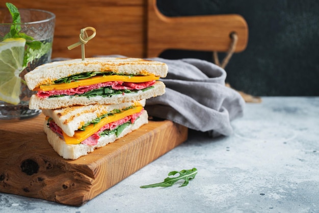 Two homemade sandwiches with sausage cheese and arugula on a light concrete background