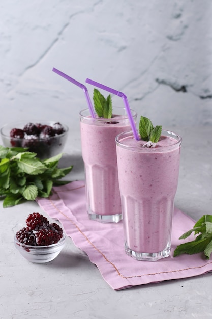 Two homemade smoothies with frozen blackberries on gray background