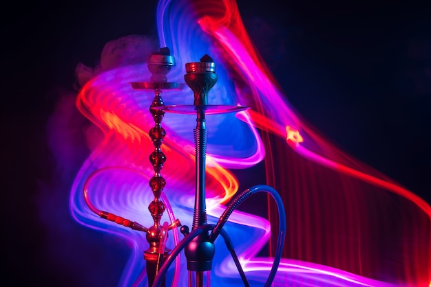 Foto due ciotole di narghilè con carboncini shisha con fumo fumoso con luci al neon rosse blu su sfondo nero