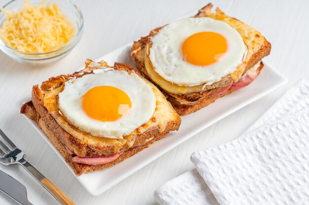 Two hot baked French sandwiches named Croque Madame with ham and cheese topped with fried egg