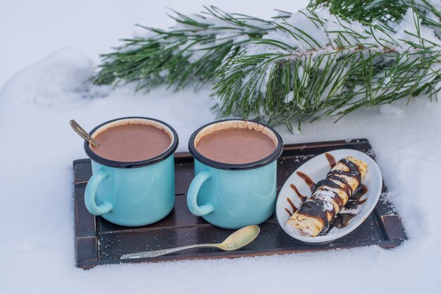 눈과 흰색 배경의 침대에 두 뜨거운 코코아 음료를 닫습니다. 크리스마스 겨울 아침의 개념