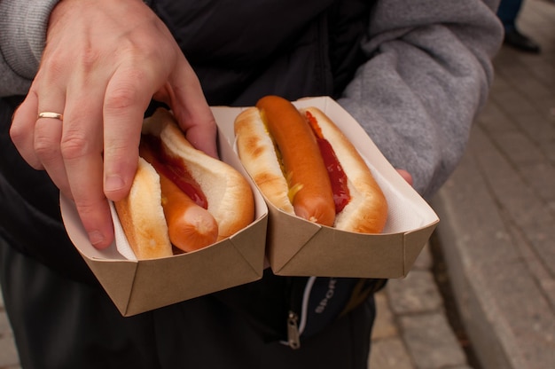 Photo two hot dogs in a cardboard box in the man's hand