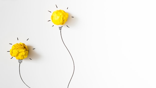 Two illuminated crumpled yellow paper light bulb on white background