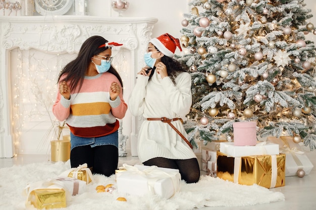 Two indian girl in eyeglasses sitting near Christmas tree