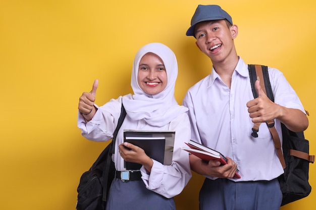 Two Indonesian high school students in white and grey uniform holding books while giving thumbs up