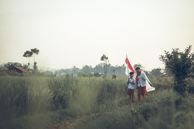 Two Indonesian school students holding flag in the rice field. Proud elementary pupil celebrating in