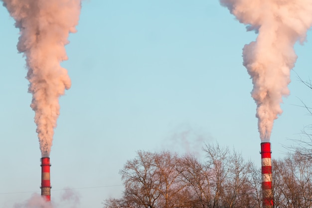 two industrial chimneys with heavy sunset pink smoke causing air pollution on the blue sky