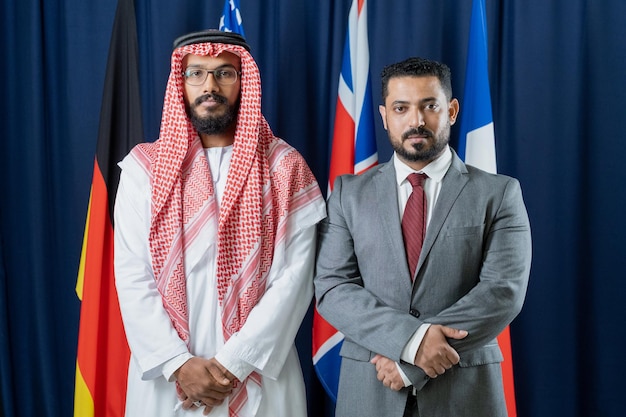 Two intercultural delegates standing against flags of countries included in g