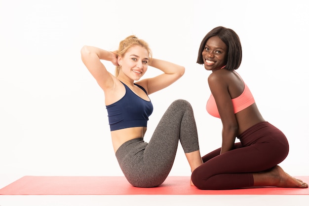 Two international muscular sportswomen doing pair exercise. Girls performing sit-ups and push-ups