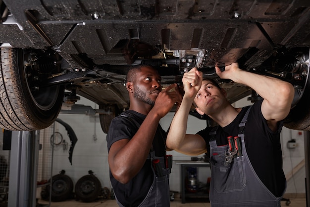 Two interracial diverse mechanics checking car bottom in auto service