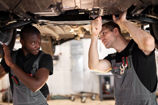 Two interracial diverse mechanics checking car bottom in auto service