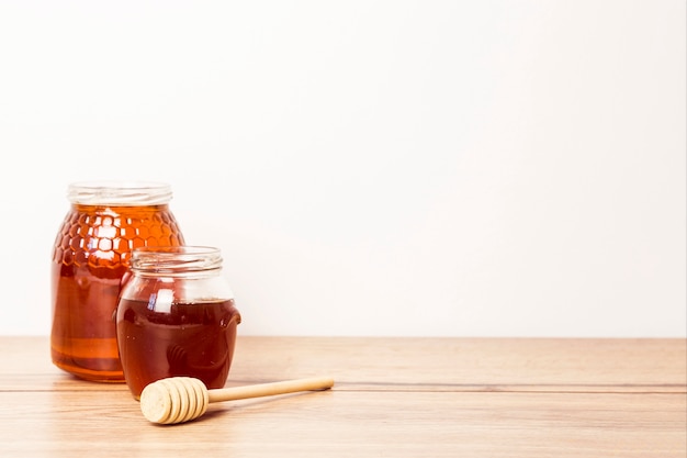 Two jar of honey with honey dipper on wooden desk