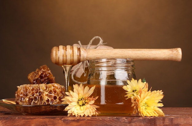 Two jars of honeyhoneycombs and wooden drizzler on table on yellow background