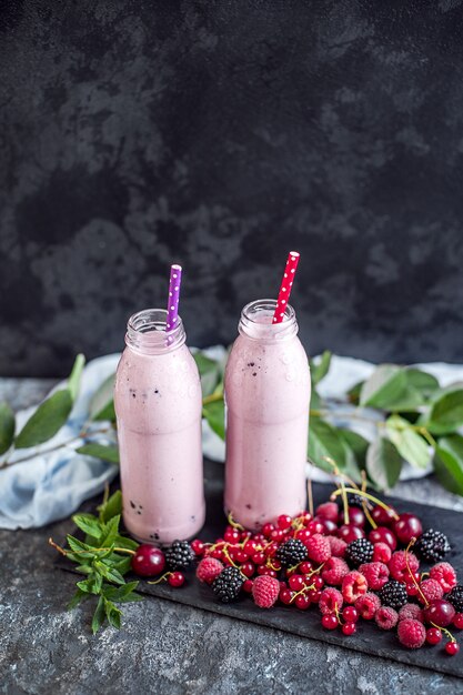 Two jars of milkshake or smoothie with cranberries, strawberries and blueberries standing on stone surface