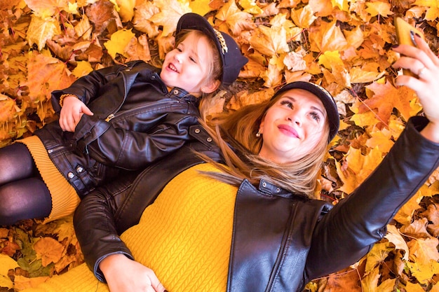 Due ragazze allegre e gioiose che prendono selfie seduti insieme nella natura autunnale