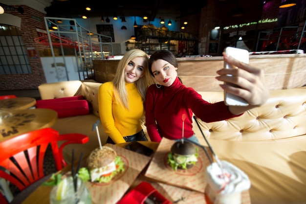 Due allegre ragazze allegre che prendono un selfie seduti insieme al caffè