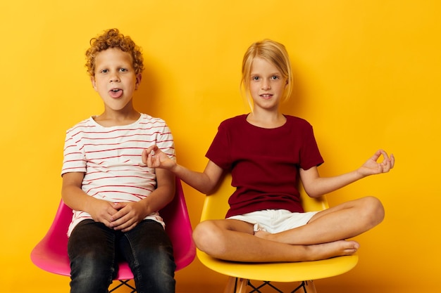 Two joyful children childhood sitting on chairs together on colored background